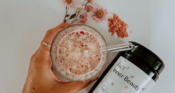 Feminine hand holding a drink. Bottle of her1 product called Inner Beauty rests beside.