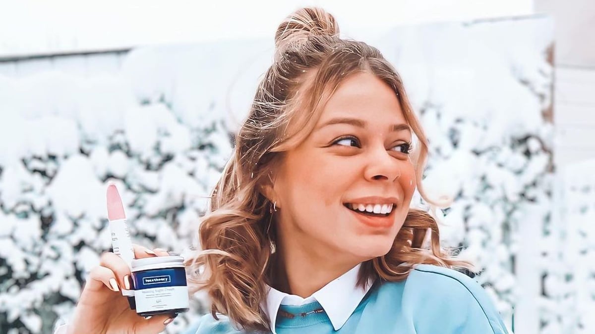 Facetheory ambassador holds 2 of their products while looking away from the camera to the right. Her hair is in a half bun and there's a snowy background behind her.