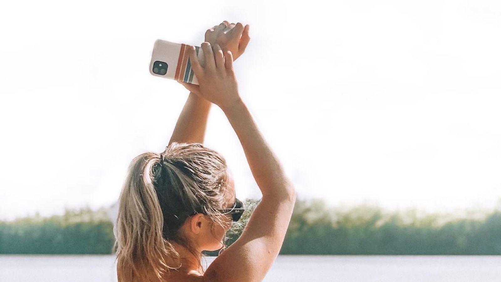 Brand ambassador @savannahwickey stand faces a lake and holds up her arms, slightly crossed. in her right hand she holds up her mobile phone with a striped Casely cover.